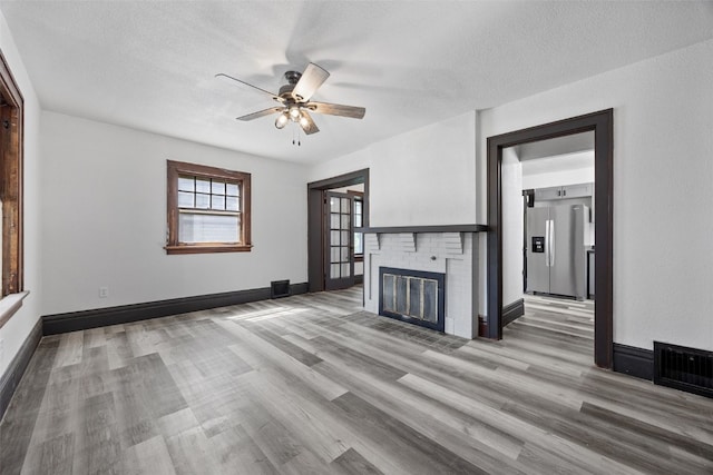 1818 Park Ave SE, Cedar Rapids, IA 52403 - unfurnished living room featuring ceiling fan, wood finished floors, a brick fireplace, and a textured ceiling