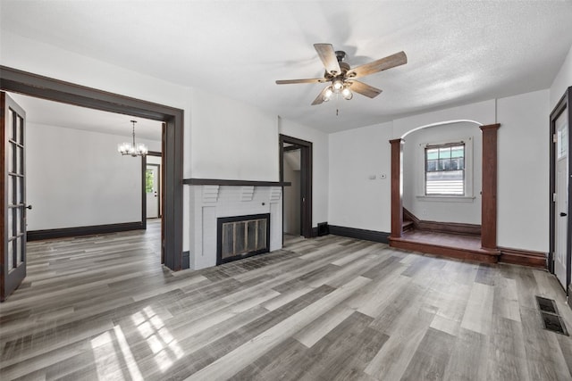 1818 Park Ave SE, Cedar Rapids, IA 52403 - unfurnished living room with a brick fireplace, light wood-style floors, a ceiling fan, arched walkways, and a chandelier