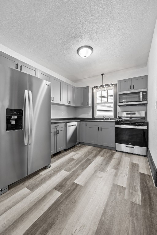 1818 Park Ave SE, Cedar Rapids, IA 52403 - kitchen featuring gray cabinetry, stainless steel appliances, a textured ceiling, dark countertops, and light wood finished floors
