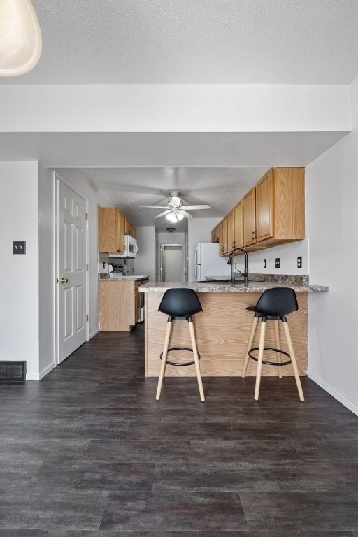 1167 74th St NE, Cedar Rapids, IA 52402 - kitchen featuring a peninsula, a kitchen breakfast bar, a ceiling fan, and dark wood-style flooring