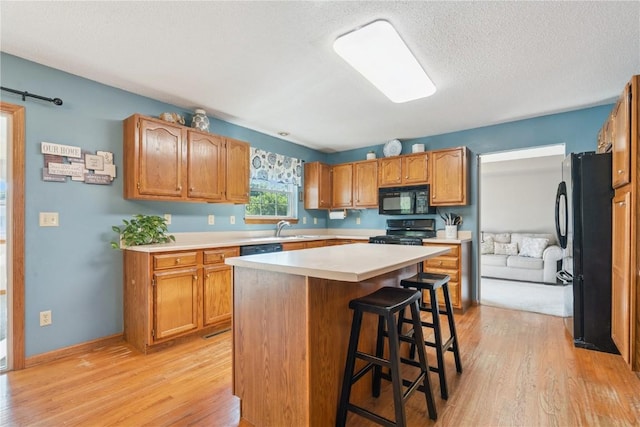 405 Stoney Creek Rd NW, Cedar Rapids, IA 52405 - kitchen with light wood finished floors, black appliances, a breakfast bar area, a center island, and light countertops