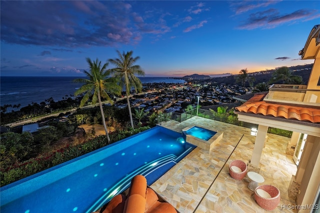 pool at dusk with a patio area, an in ground hot tub, and a water view