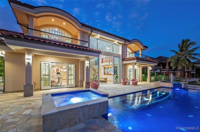 rear view of property featuring a patio, pool water feature, a balcony, and a swimming pool with hot tub