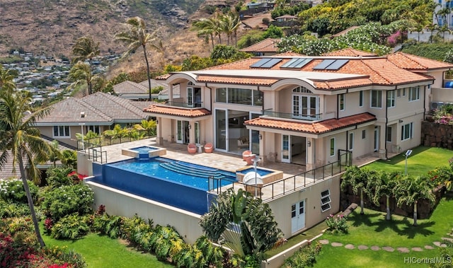 back of property featuring a swimming pool with hot tub, a patio, a lawn, and a balcony