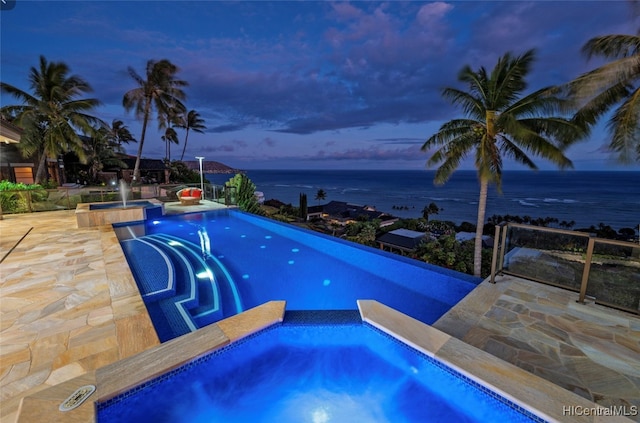 pool at dusk featuring a water view, an in ground hot tub, and a patio area