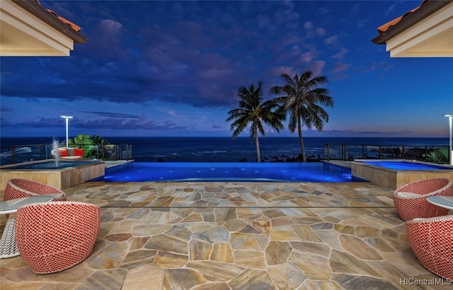 pool at dusk with a patio, an in ground hot tub, pool water feature, and a water view