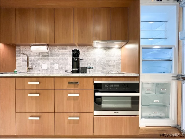 kitchen with oven, decorative backsplash, light stone counters, and sink