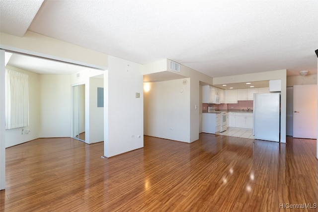 unfurnished living room with sink, a textured ceiling, and light wood-type flooring