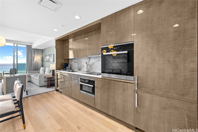 kitchen featuring a water view, light hardwood / wood-style floors, stainless steel oven, and decorative backsplash