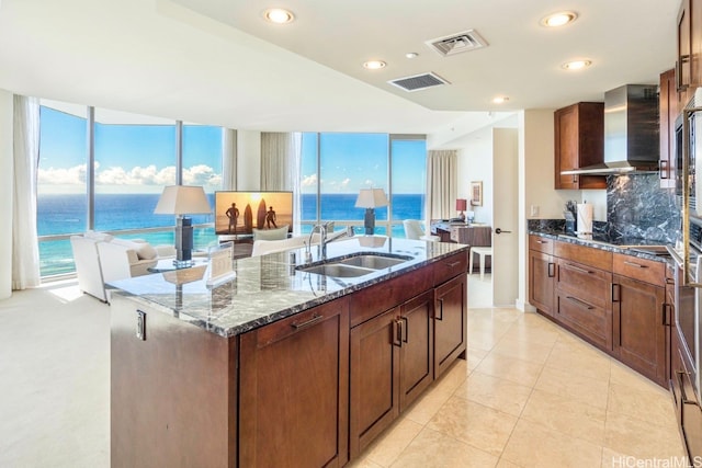 kitchen featuring wall chimney range hood, sink, a wealth of natural light, a water view, and a center island with sink