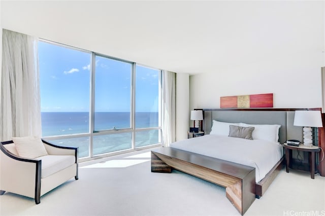 bedroom featuring a water view, light colored carpet, and floor to ceiling windows