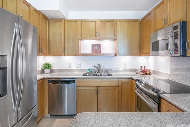 kitchen with light tile patterned floors, stainless steel appliances, light stone countertops, and sink