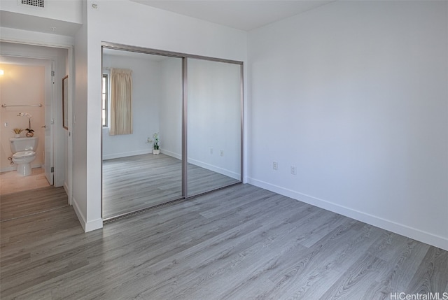 unfurnished bedroom featuring a closet, light hardwood / wood-style floors, and connected bathroom