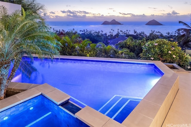 pool at dusk with a hot tub and a water view