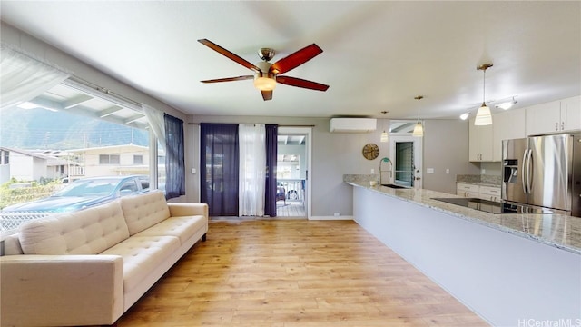 living room featuring ceiling fan, sink, a wall mounted AC, and light wood-type flooring