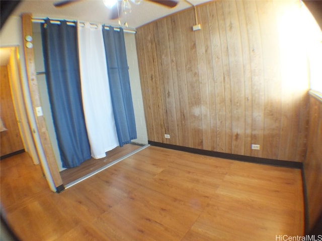 empty room featuring ceiling fan, wood-type flooring, and wooden walls