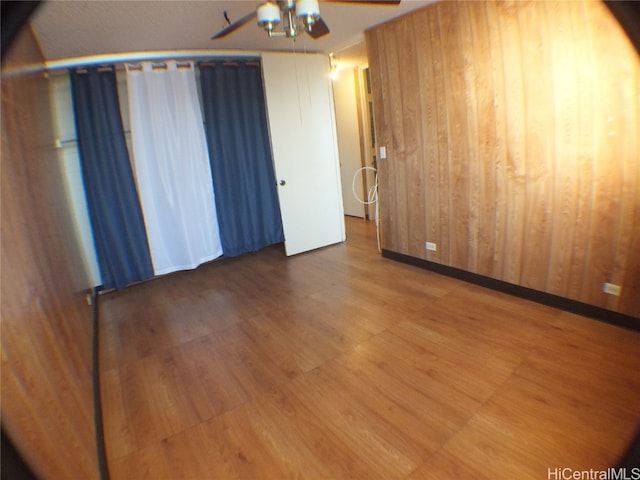 unfurnished room featuring ceiling fan, wooden walls, and hardwood / wood-style floors