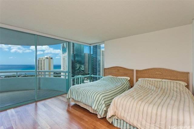 bedroom featuring a water view, floor to ceiling windows, a city view, and wood finished floors