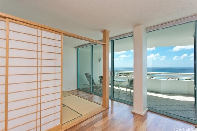 interior space featuring expansive windows, a textured ceiling, a water view, and wood finished floors