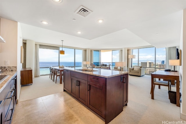 kitchen featuring sink, light colored carpet, decorative light fixtures, light stone counters, and a water view