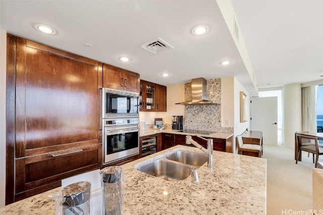 kitchen with wall chimney range hood, sink, appliances with stainless steel finishes, light stone countertops, and wine cooler