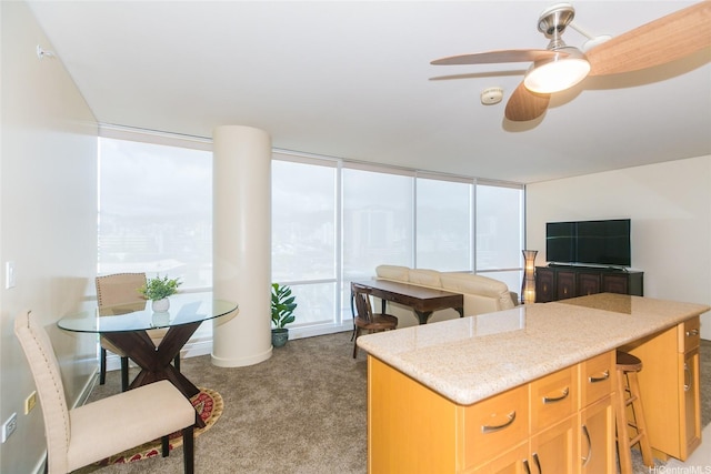 kitchen featuring a ceiling fan, light colored carpet, expansive windows, a center island, and light stone countertops