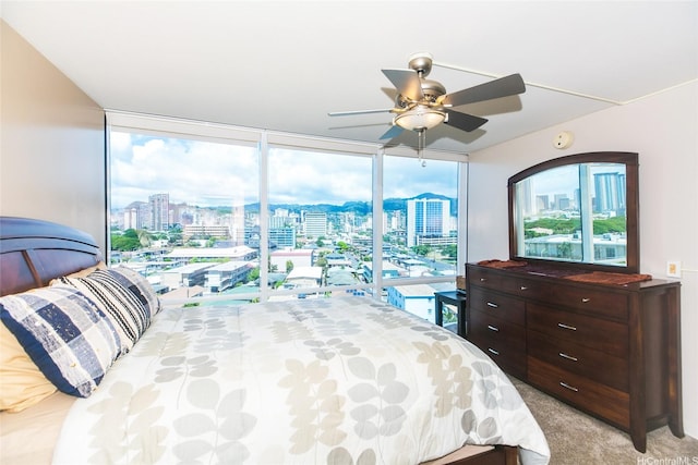 bedroom with a city view, floor to ceiling windows, light carpet, and ceiling fan
