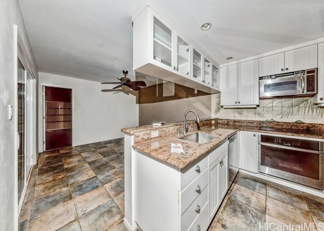 kitchen with light stone countertops, appliances with stainless steel finishes, sink, ceiling fan, and white cabinets