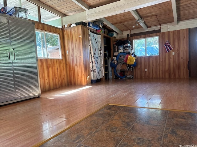spare room with beamed ceiling, wooden walls, wood finished floors, and ceiling fan