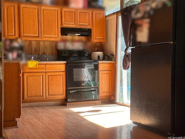 kitchen featuring under cabinet range hood, light wood-style floors, brown cabinets, and black appliances