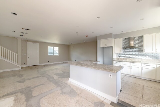 kitchen featuring a center island, white cabinetry, wall chimney exhaust hood, stovetop, and decorative backsplash