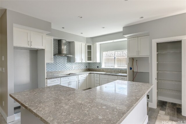 kitchen featuring wall chimney range hood, white cabinetry, a center island, and stovetop