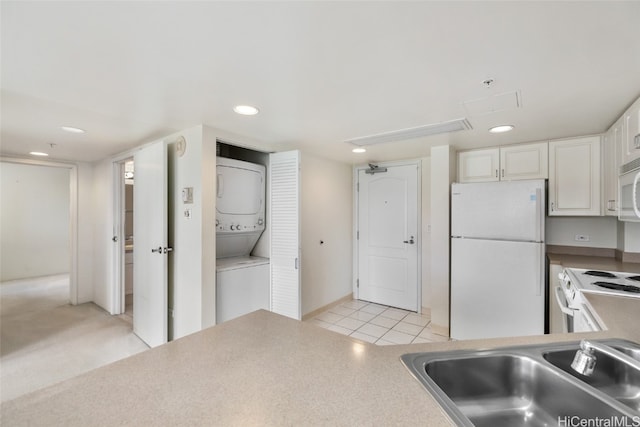 kitchen featuring white appliances, sink, white cabinetry, stacked washer and dryer, and light tile patterned floors