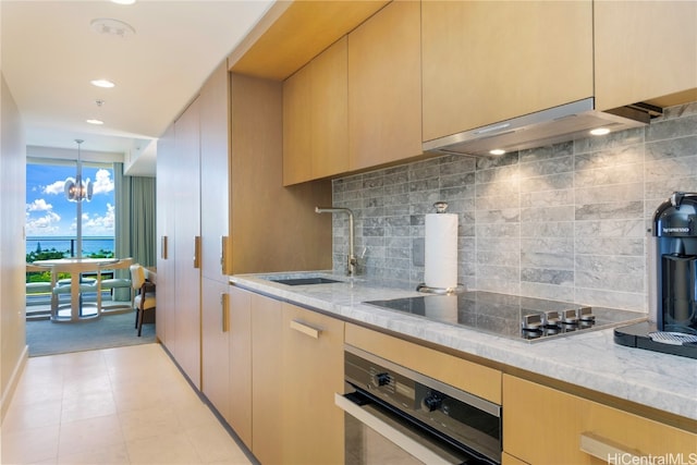 kitchen with decorative backsplash, stainless steel oven, an inviting chandelier, light brown cabinetry, and black electric stovetop