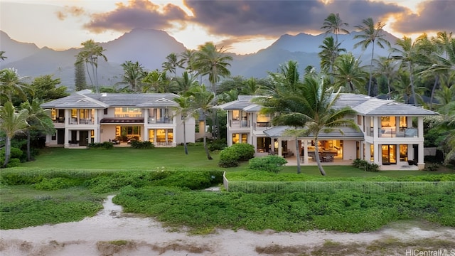 back house at dusk with a patio, a mountain view, a lawn, and a balcony