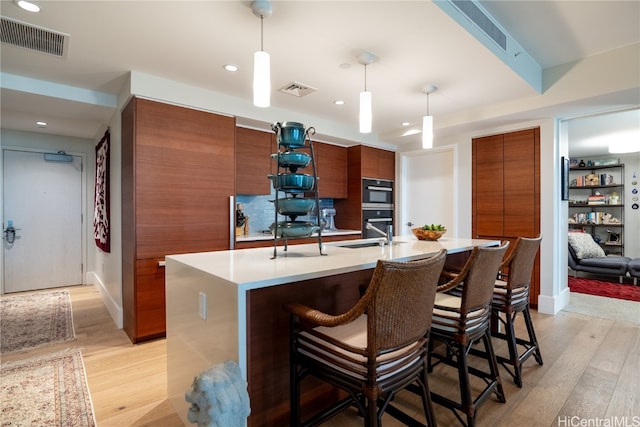 kitchen with light hardwood / wood-style floors, a center island with sink, a kitchen breakfast bar, and pendant lighting