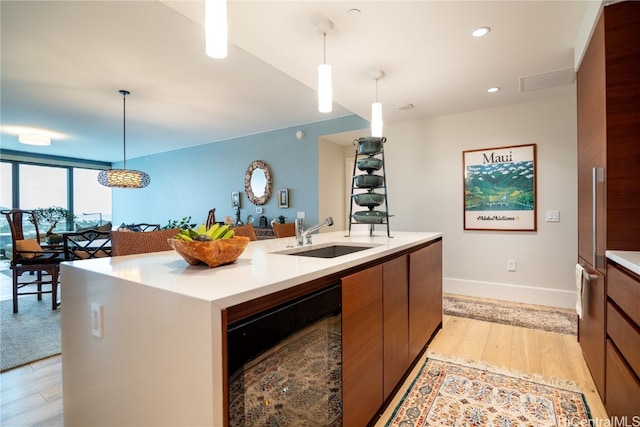 kitchen with sink, light wood-type flooring, decorative light fixtures, wine cooler, and a center island with sink