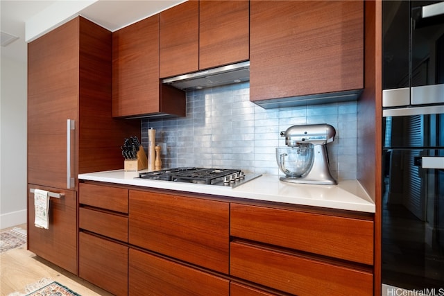 kitchen featuring tasteful backsplash, black oven, light hardwood / wood-style flooring, range hood, and stainless steel gas cooktop