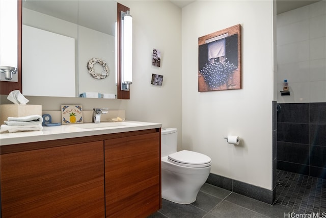 bathroom with toilet, vanity, a tile shower, and tile patterned flooring