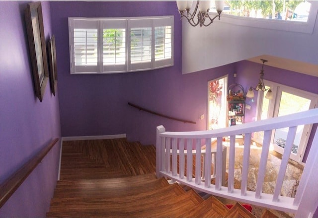 stairway with a wealth of natural light, a notable chandelier, and parquet floors