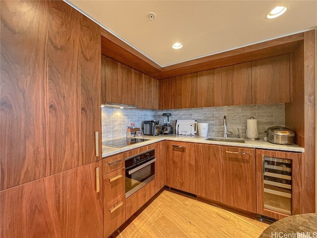 kitchen with black electric stovetop, sink, stainless steel oven, light hardwood / wood-style floors, and wine cooler