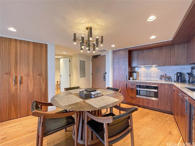 dining area with light hardwood / wood-style flooring, electric panel, and a notable chandelier