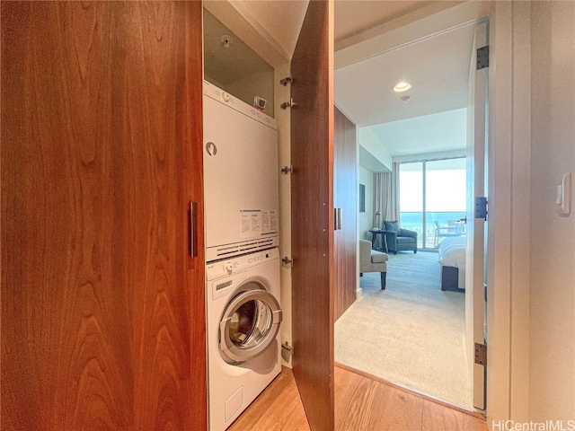 clothes washing area with light hardwood / wood-style floors, stacked washer / dryer, and a water view