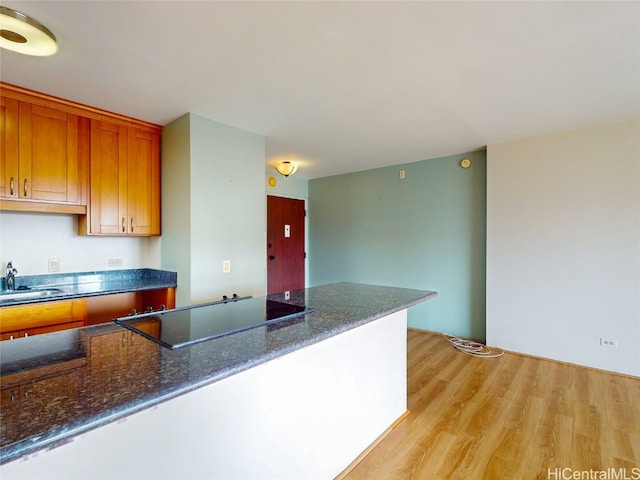 kitchen featuring black electric stovetop, light hardwood / wood-style floors, sink, and dark stone counters