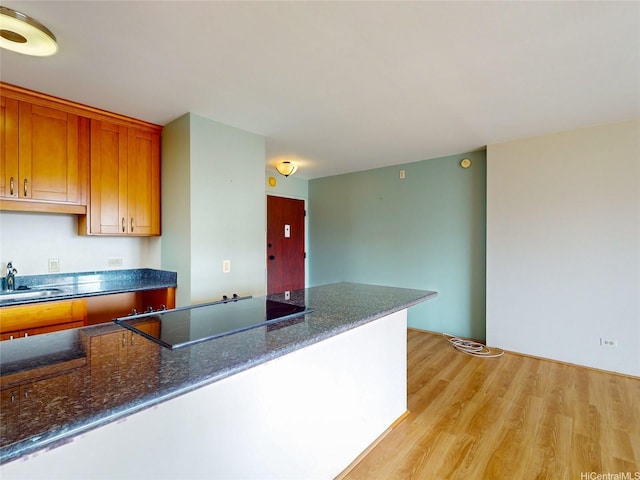 kitchen featuring brown cabinets, a sink, dark stone countertops, black electric stovetop, and light wood-style floors