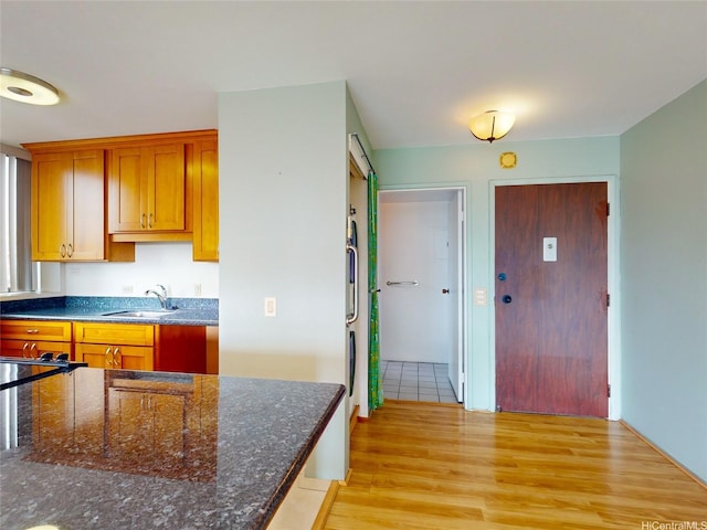 kitchen featuring a sink, dark stone counters, and light wood-style flooring