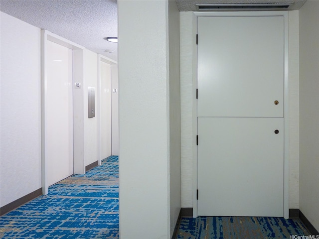 hall with carpet floors, elevator, and a textured ceiling