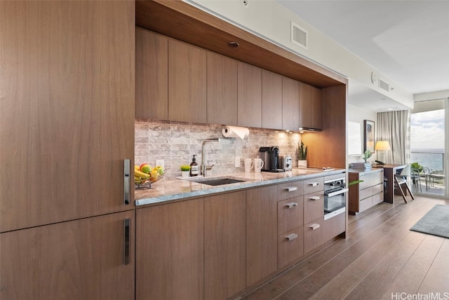 kitchen featuring stainless steel oven, dark hardwood / wood-style floors, backsplash, sink, and light stone counters