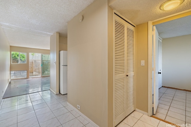 hall with a textured ceiling and light tile patterned floors