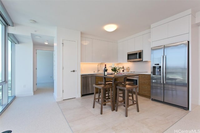 kitchen featuring a kitchen bar, stainless steel appliances, sink, white cabinets, and a kitchen island